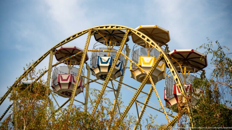 Small Ferris wheel with colorful gondolas in a park setting in Almaty.