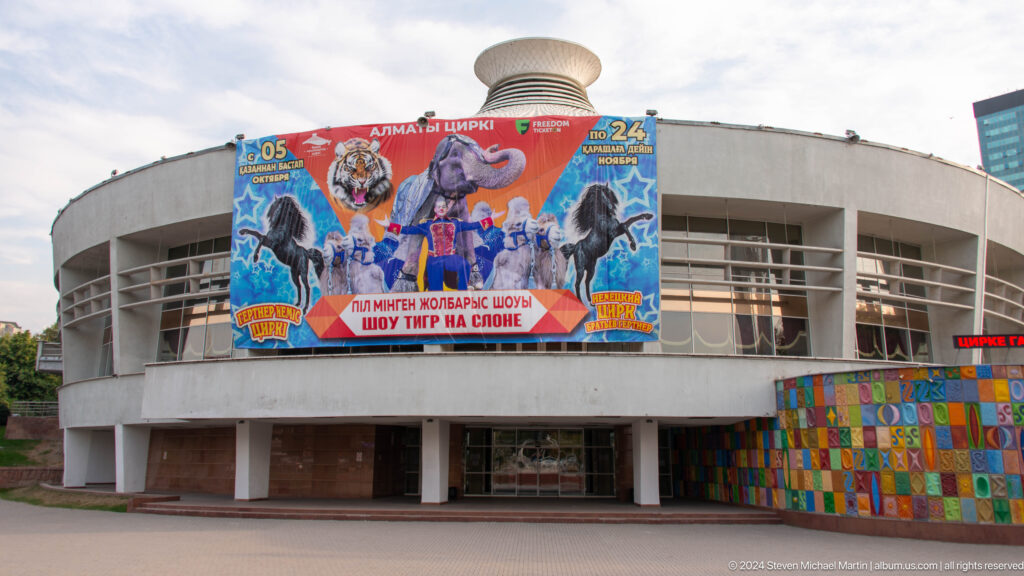 Circular sports venue in Almaty with a large colorful wrestling banner covering its exterior facade.