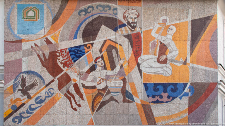 Exterior mosaic in Almaty showing stylized figures of a scholar, a scientist with glassware, a horse and rider, and an eagle in a bold abstract composition.