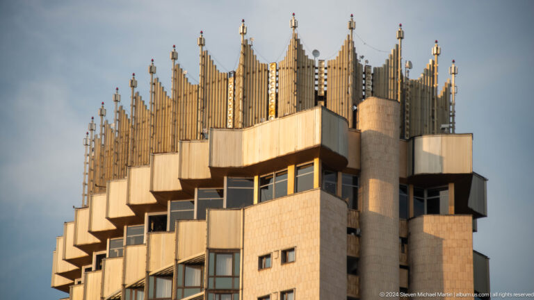 Close-up view of the upper floors and ornate crowned rooftop of a Soviet-era high-rise building in Almaty, Kazakhstan.