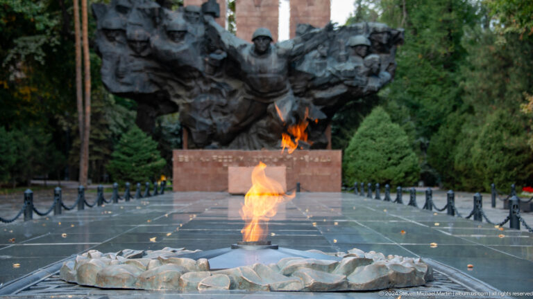 Eternal flame in sharp focus with a heroic war memorial sculpture blurred in the background in Almaty, Kazakhstan.