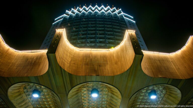 Close view of a golden sculptural canopy beneath a dark tower, an ornamental modern facade in Almaty, Kazakhstan.