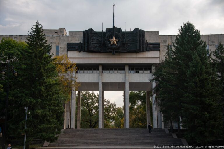 Soviet-era monumental park gateway in Almaty with tall columns and a sculptural panel topped by a red star emblem.