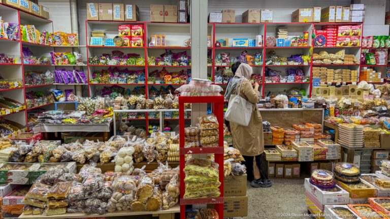 Supermarket aisle densely stocked with packaged foods inside an indoor grocery market in Almaty, Kazakhstan.