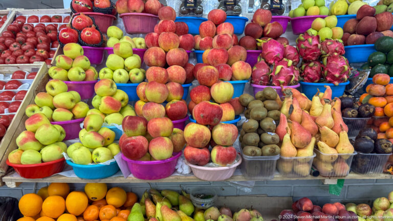 Close-up of a fruit stall in an Almaty market with apples, pears, and pomegranates arranged in dense, colorful piles.