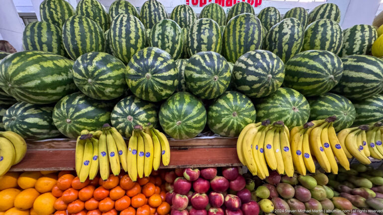 Stacked watermelons above bananas and onions at a market stall in Almaty, Kazakhstan.