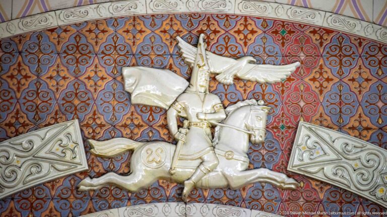 Relief sculpture of a rider on a rearing winged horse set into a patterned wall panel in Almaty, Kazakhstan.