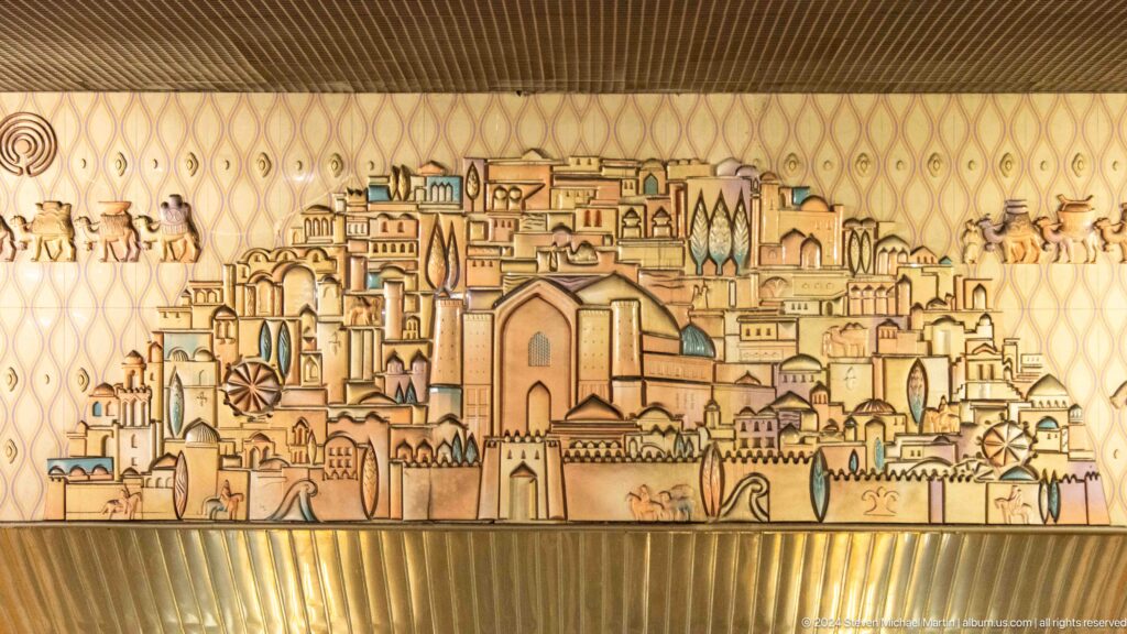 Line-drawn Almaty cityscape mural on a gold wall, depicting a dense historic skyline with domes and towers.