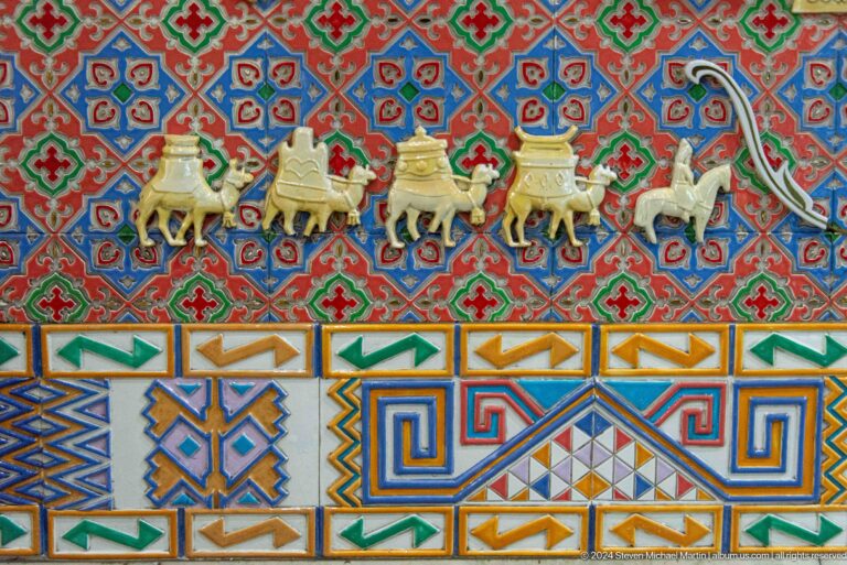 Decorative tapestry showing a line of camels in a caravan framed by geometric border patterns.