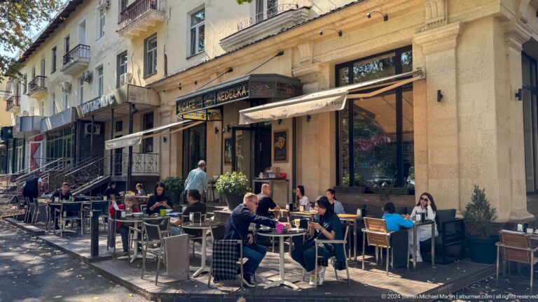 Outdoor café tables crowded with diners along a city sidewalk in Almaty, Kazakhstan.