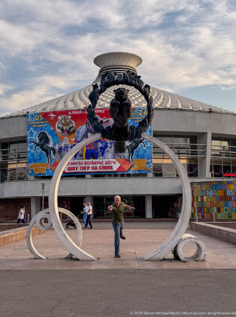 Man standing inside a large circular sculpture in front of a circus banner in Almaty, Kazakhstan.