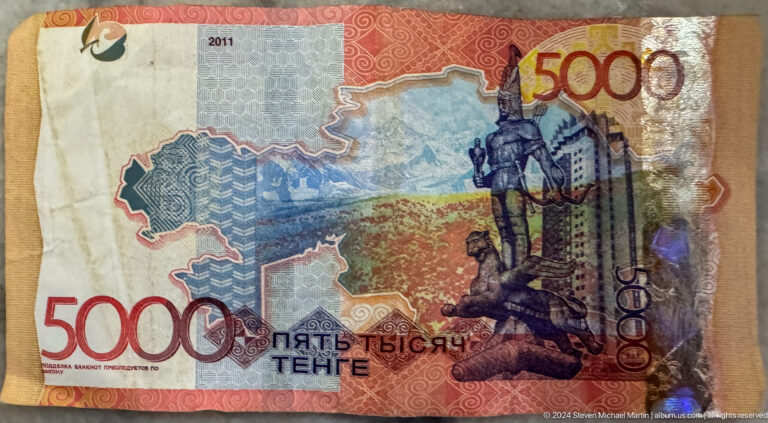 Close-up of a Kazakhstan 5000 tenge banknote showing detailed monument imagery and intricate printed patterns.