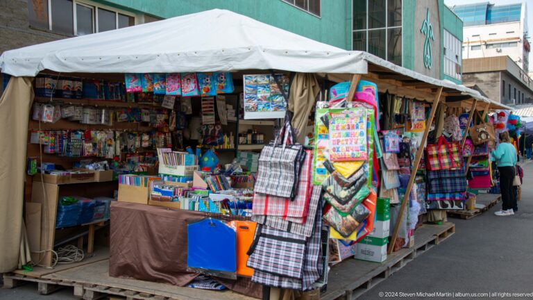 Open-air book and news kiosk in Almaty, Kazakhstan, with shelves densely packed with books and printed materials.