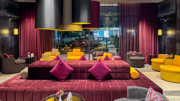 Contemporary hotel lobby lounge with magenta sofas, colorful cushions, and low tables in Almaty.