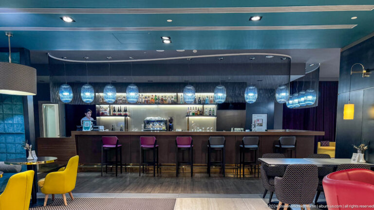 Modern hotel bar and lounge with globe pendant lights, bar counter, and seating area in Almaty.