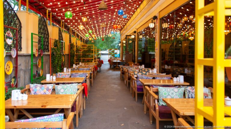 Covered restaurant terrace in Almaty with rows of wooden tables arranged in a decorated outdoor dining area.