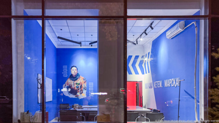 Man behind a blue-lit reception desk in a hotel lobby in Almaty, Kazakhstan.
