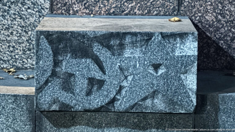 Carved stone relief block featuring stylized animal figures installed as public art in an outdoor setting at night.