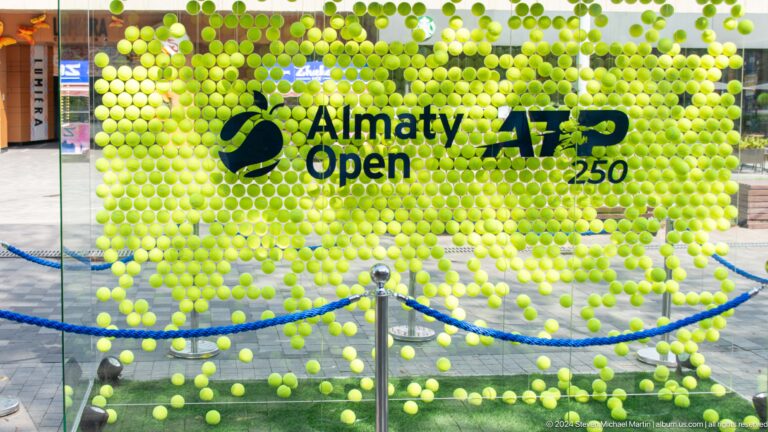 Green tennis-ball wall installation with the words Almaty Open ATP 250 in white letters.