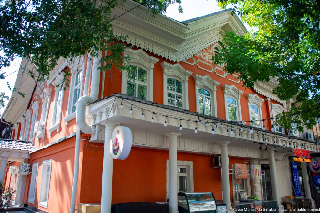 Ornate red-and-white historic corner building along a city street in Almaty.