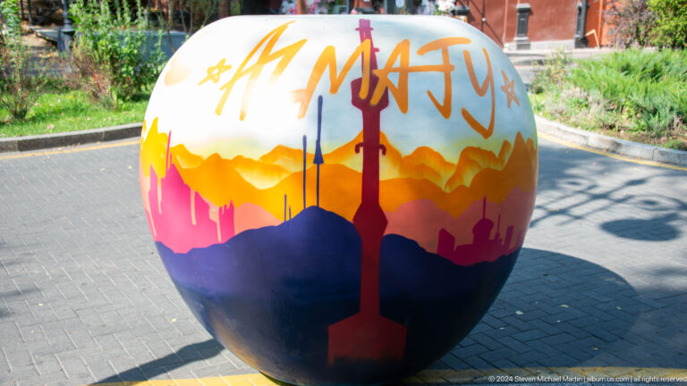 Painted spherical public art sculpture depicting the Almaty skyline in an outdoor urban setting.