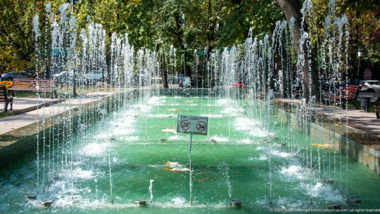 Close view of vertical water jets rising from a green-tinted fountain pool in a park in Almaty, Kazakhstan.