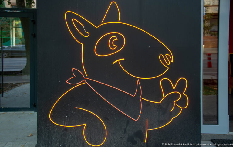 Yellow line drawing of a cartoon animal on a dark street panel in Almaty, Kazakhstan.