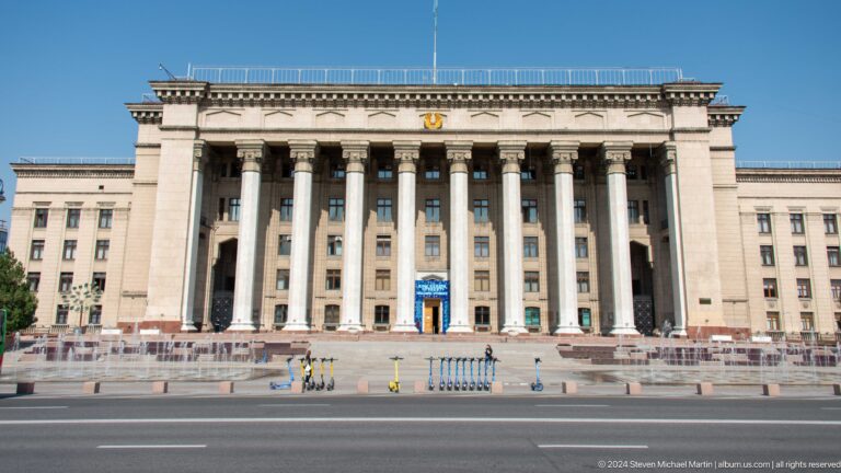 Neoclassical public building in Almaty, Kazakhstan, with tall columns and a blue entrance door.
