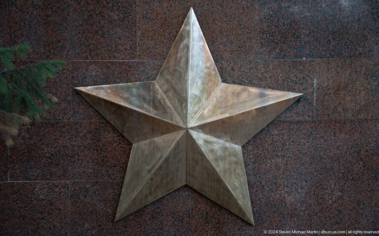 Close view of a five-pointed faceted metal star fixed to a polished stone wall, part of a memorial emblem in Almaty, Kazakhstan.