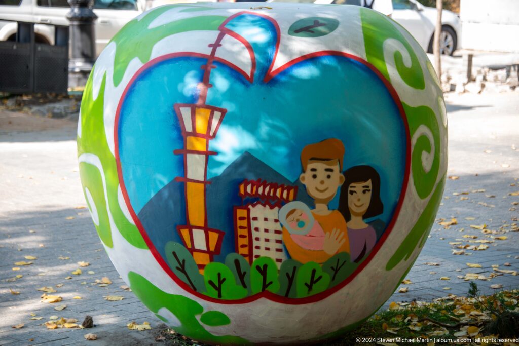 Painted spherical sculpture in Almaty featuring a family and city skyline motif in an outdoor public area.