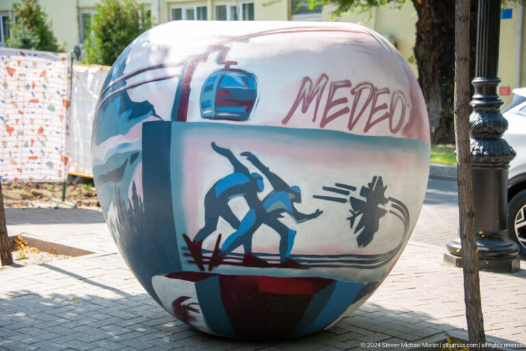 Colorfully painted spherical sculpture with abstract figures and writing installed in a public space.