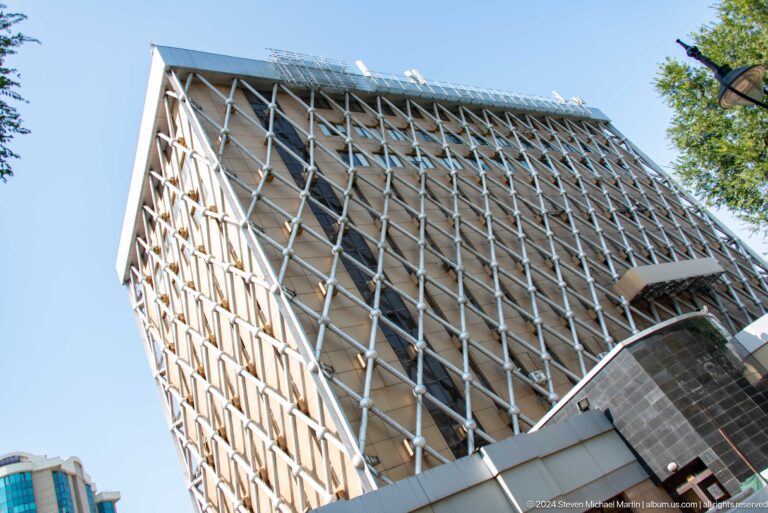 Low-angle view of a modern office building in Almaty, Kazakhstan, with an exposed diagonal lattice facade.