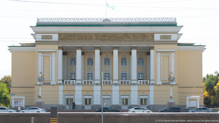 Front view of the Abai Kazakh State Academic Opera and Ballet Theatre in Almaty, a neoclassical building with tall white columns and a decorative frieze.