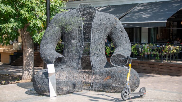 Large dark abstract stone sculpture beside a scooter in a public space in Almaty, Kazakhstan.