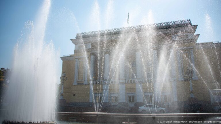 Opera house in Almaty seen through tall jets of a public fountain in the foreground.