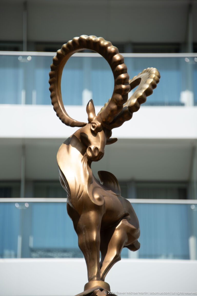 Bronze winged snow leopard sculpture with spread wings set on a pedestal in an urban public space.