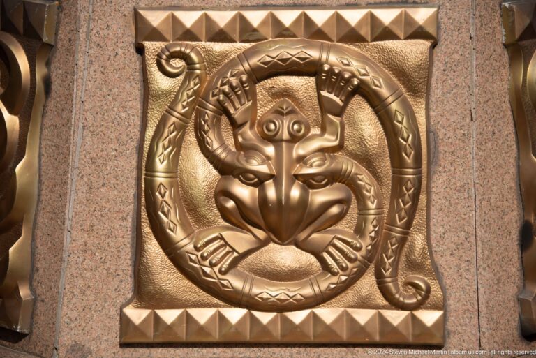 Bronze circular relief featuring a stylized animal face in an ornamental medallion design.