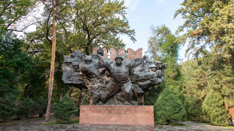 Wide view of the Panfilov Park war memorial’s bronze heroic figures set in a wooded park in Almaty, Kazakhstan.