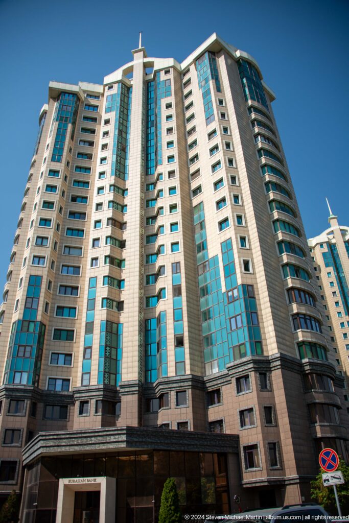 Tall beige apartment towers with blue glass windows clustered closely together in modern Almaty.