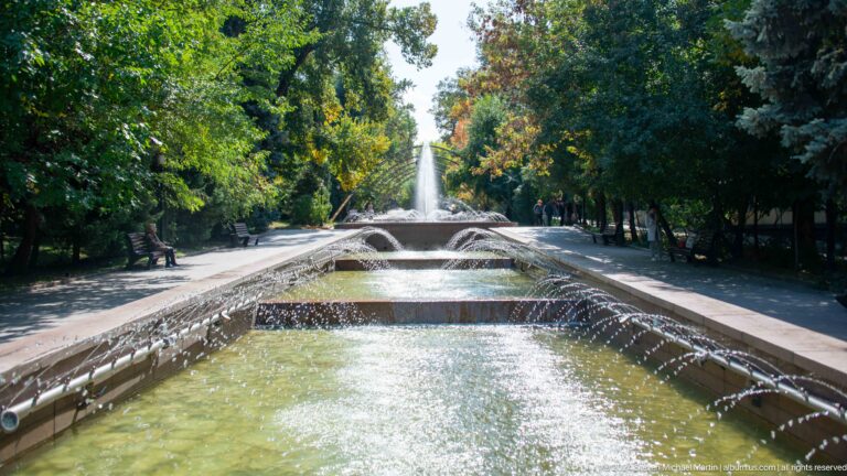 Long formal public fountain beneath rows of trees in Almaty, Kazakhstan, viewed along its central axis.