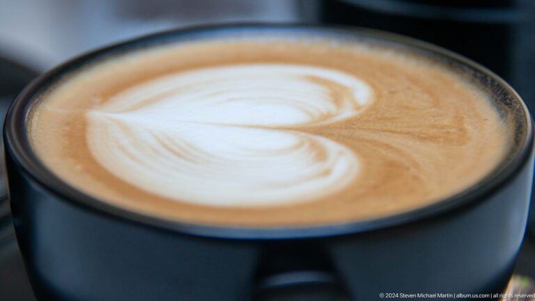 Close-up of a latte in a white cup with heart-shaped foam art on top.