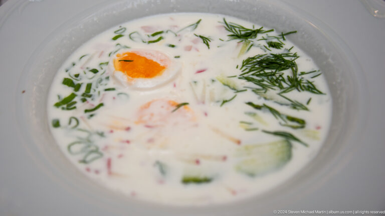 Bowl of cold soup with chopped egg and herbs on top, set on a table in Almaty.