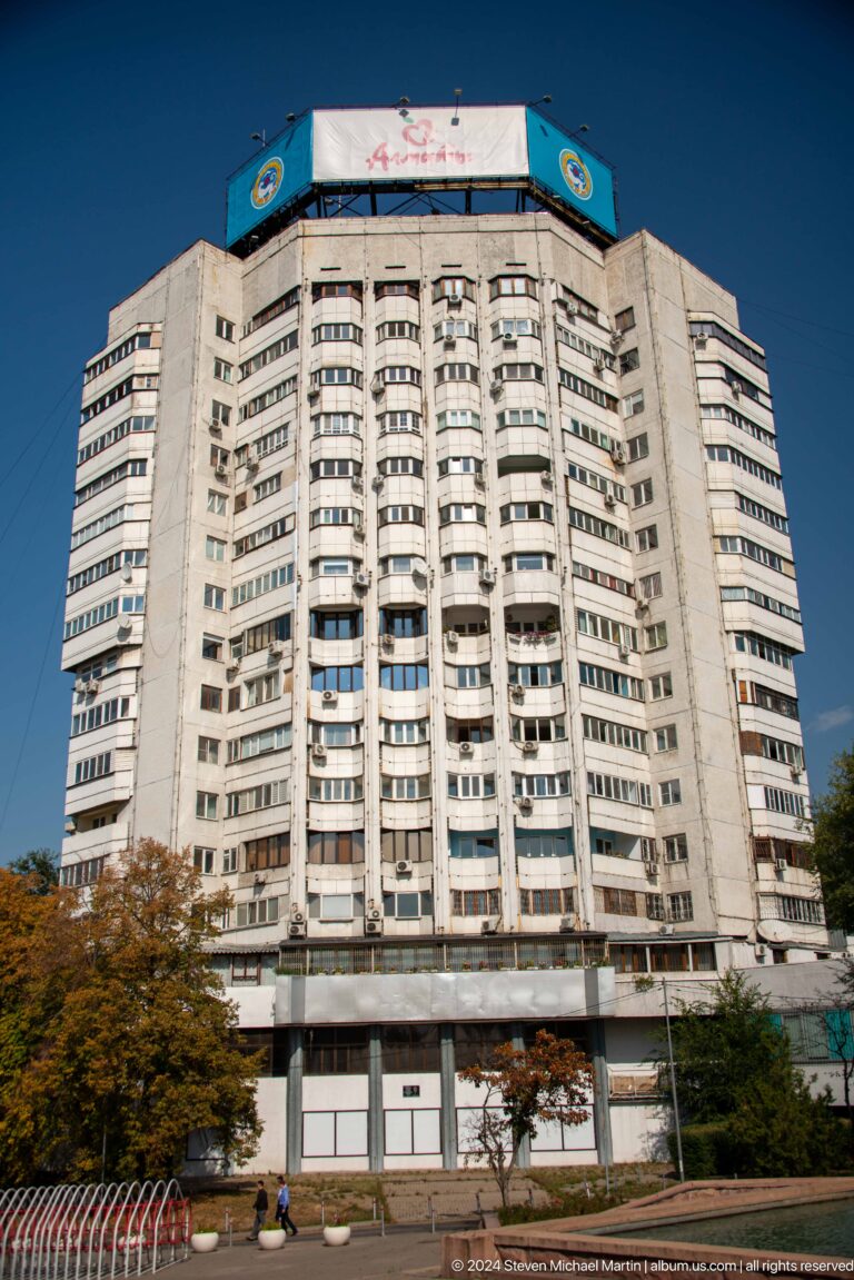 Rounded high-rise apartment building in Almaty, Kazakhstan, with many stacked balconies on its curved facade.