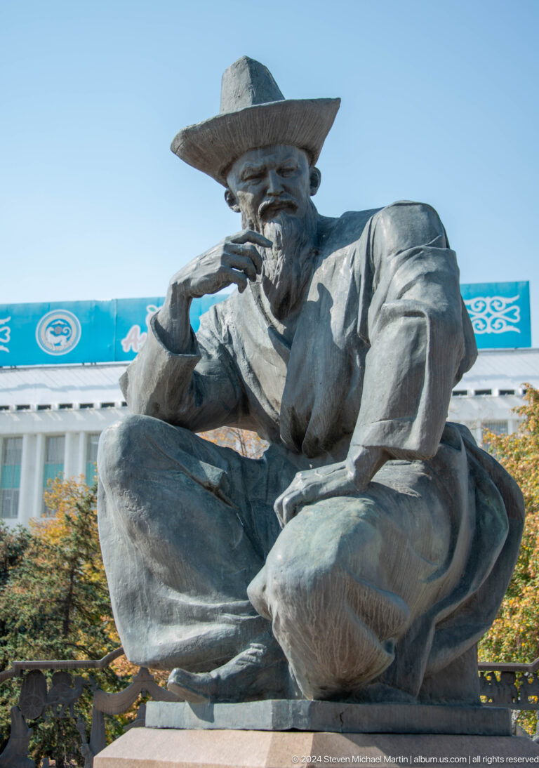 Bronze seated male statue in Almaty, Kazakhstan, shown in a contemplative pose with his head resting on his hand.