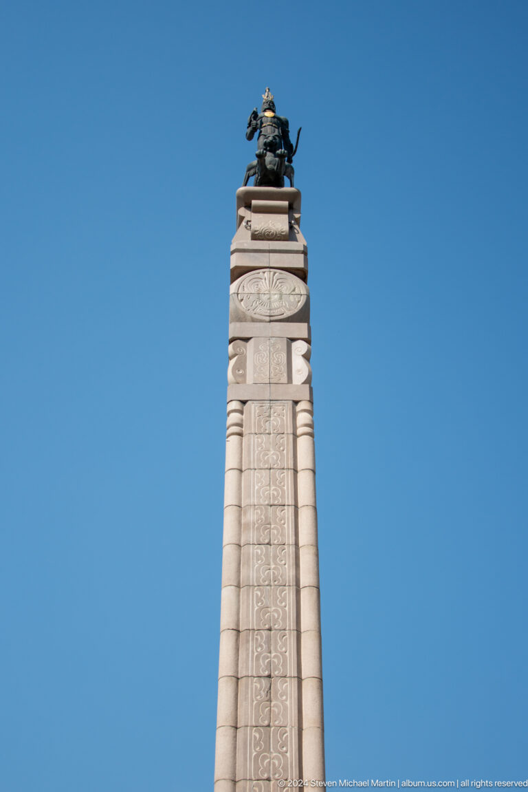 Tall carved stone memorial pillar in a public monument setting in Almaty, Kazakhstan.