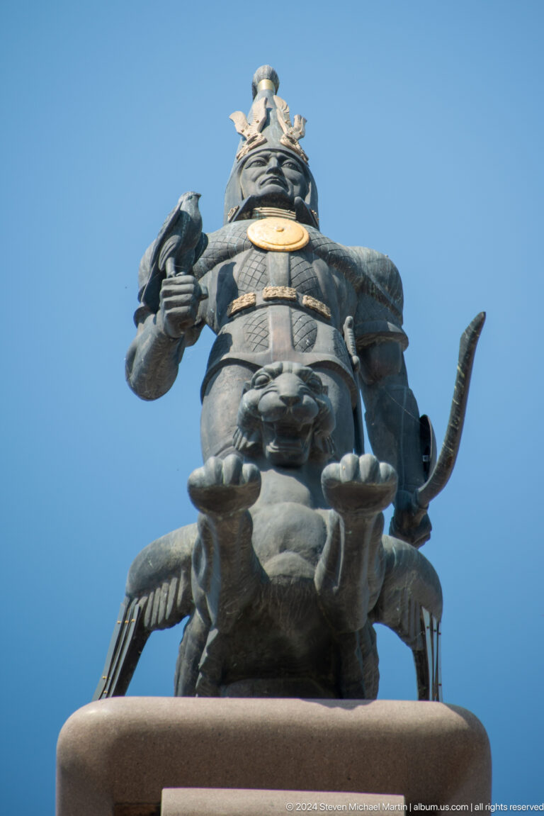 Close-up of the Golden Warrior monument in Almaty showing a bronze warrior torso with a lion figure and a bow.