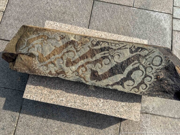 Medium view of a long stone slab carved with running animal forms, displayed in the Central State Museum of Kazakhstan in Almaty.