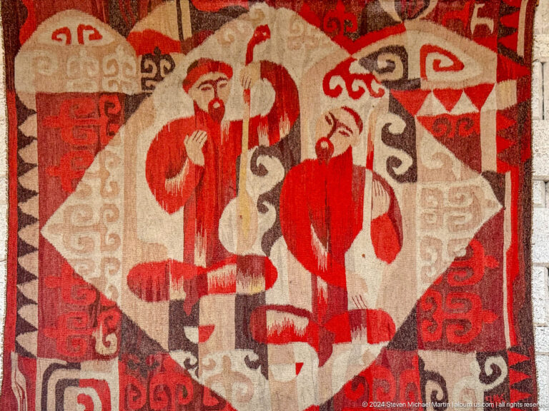 Medium view of a red and cream ornamental felt applique with stylized figures on display in the Central State Museum of Kazakhstan in Almaty.