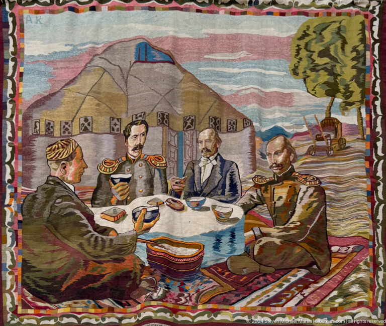 Textile artwork of a historical political meeting with officials and soldiers seated around a table, displayed at the Central State Museum of Kazakhstan in Almaty.
