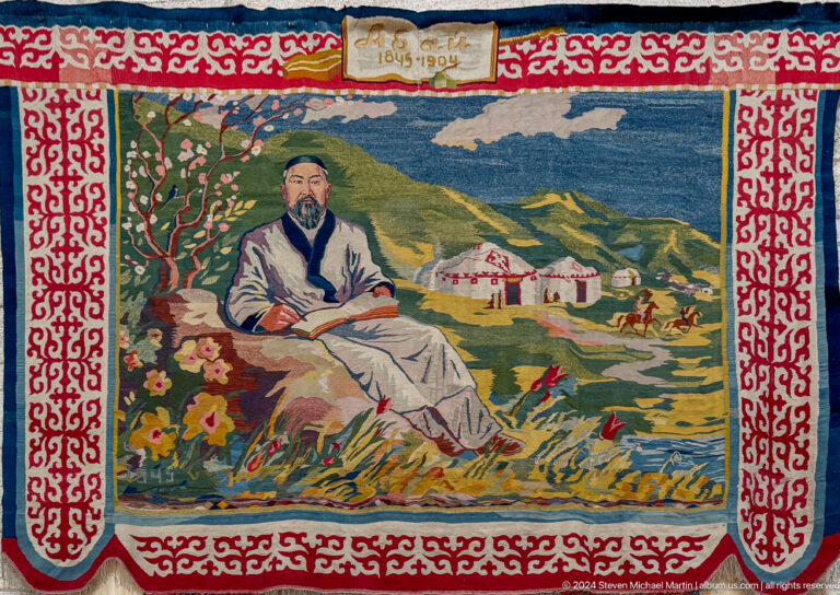 Embroidered portrait textile of a seated man displayed against a red backing in the Central State Museum in Almaty, Kazakhstan.